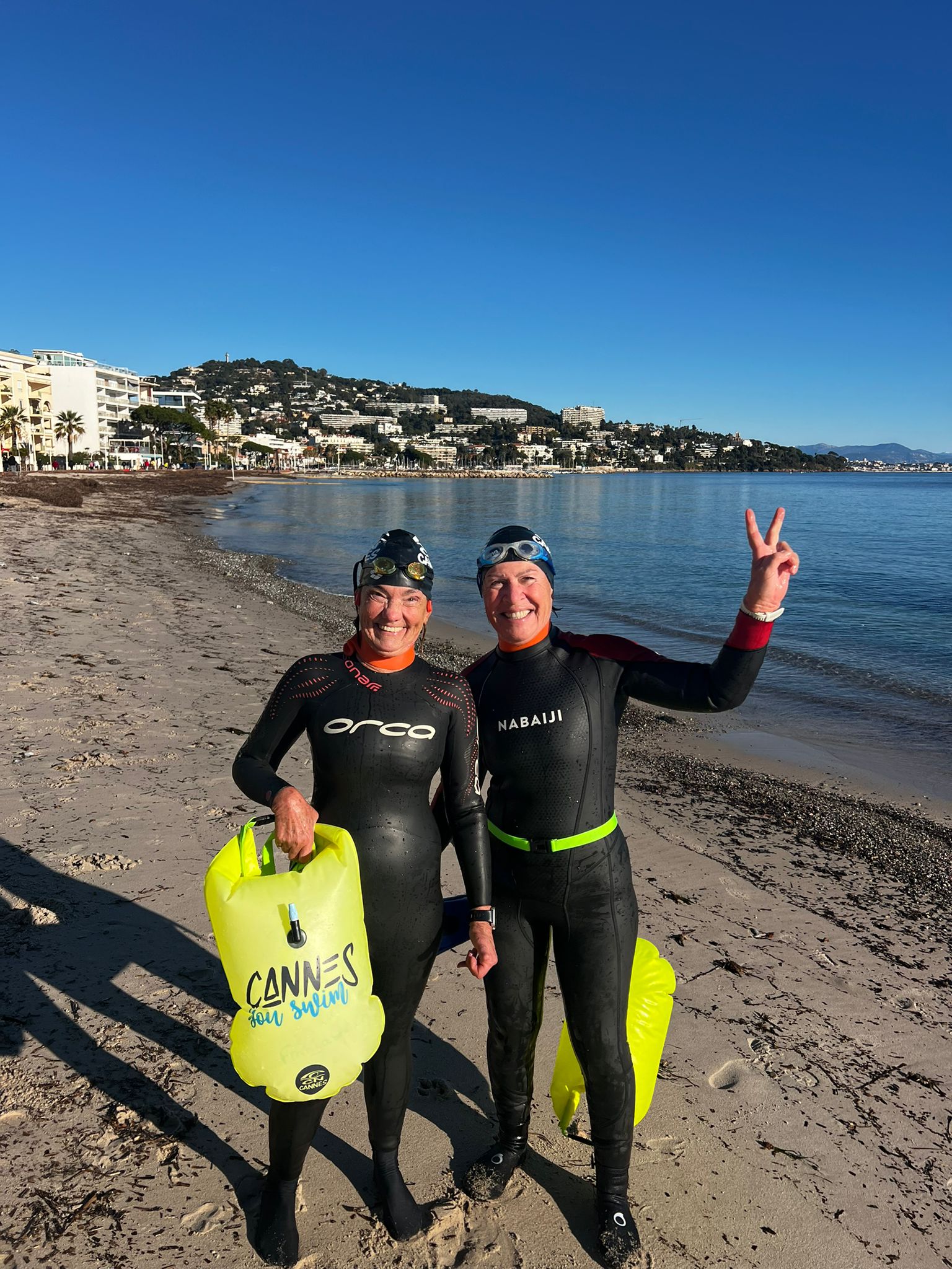 Deux nageuses en combinaison sur une plage à Cannes, avec leurs bouées de nage.