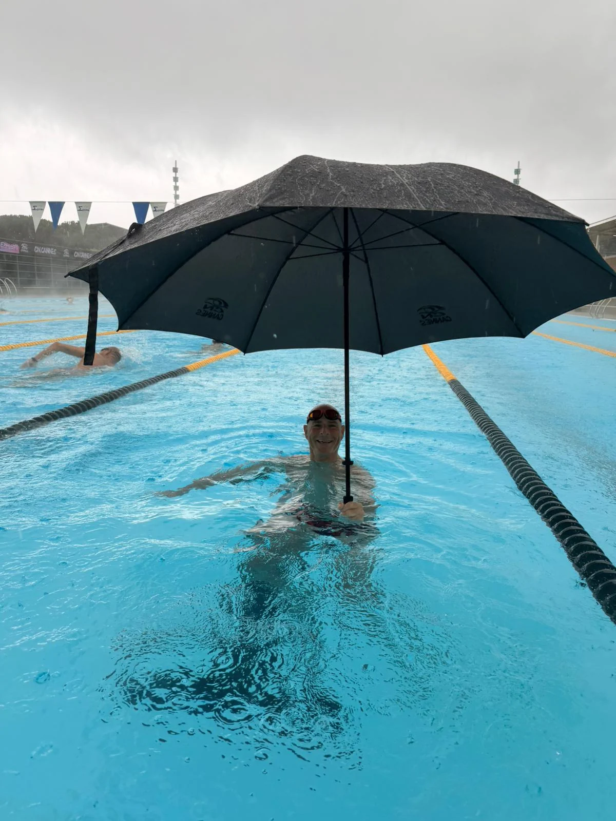 Philippe sourit dans un bassin en tenant un parapluie.